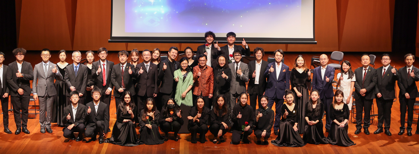 Group of people in formal attire posing and giving thumbs up in front of a screen on stage.